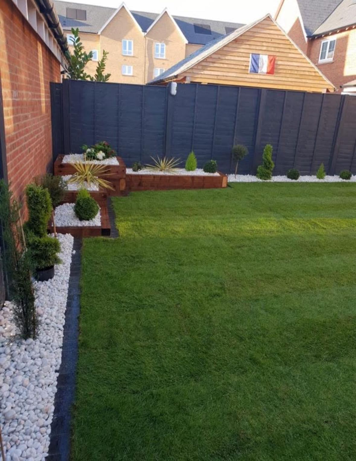 Contemporary garden with artificial turf, raised timber planters, and decorative stones